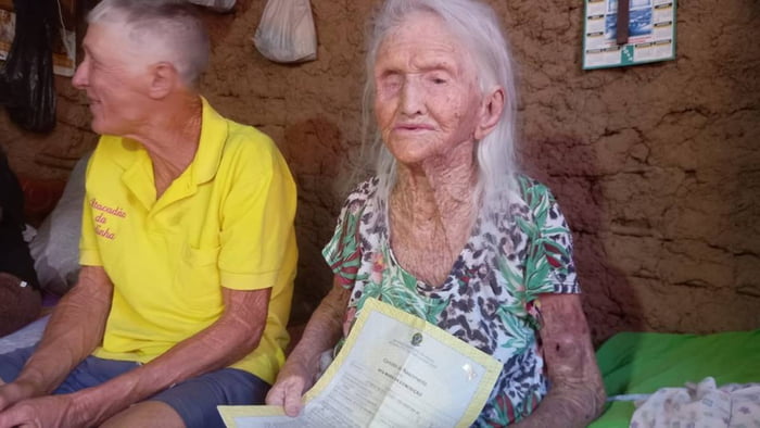 Idosa de 116 anos segura certidão de nascimento ao lado do filho de 61