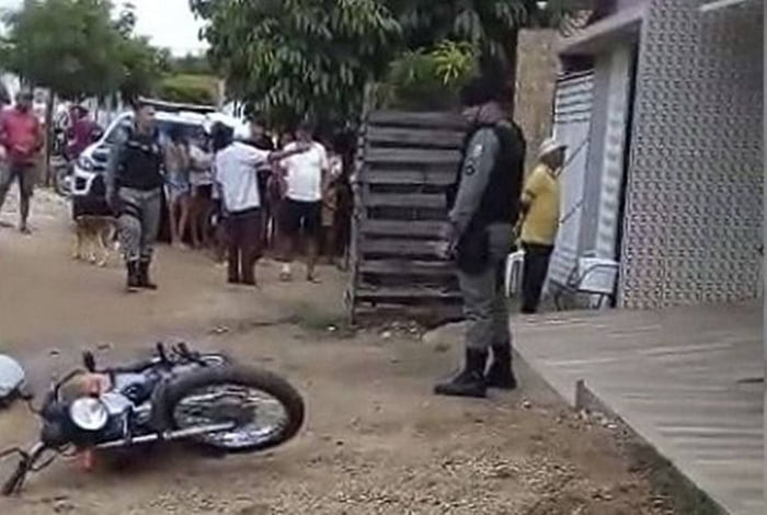 foto colorida de moto caída no chão, dois policiais em pé e pessoas em volta