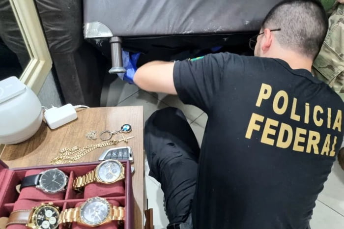 Policial federal vasculha sofá na procura de itens suspeitos durante a Operação Fair Play, no Amazonas. Em mesa ao lado, várfios relógios, correntes e controle de carro - Metrópoles