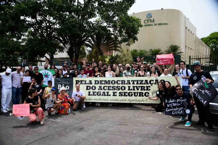 protestantes posam para foto em frente à sede do CFM, em Brasília, eles seguram uma faixa na qual está escrito "pela democratização do acesso livre, legal e seguro" da maconha