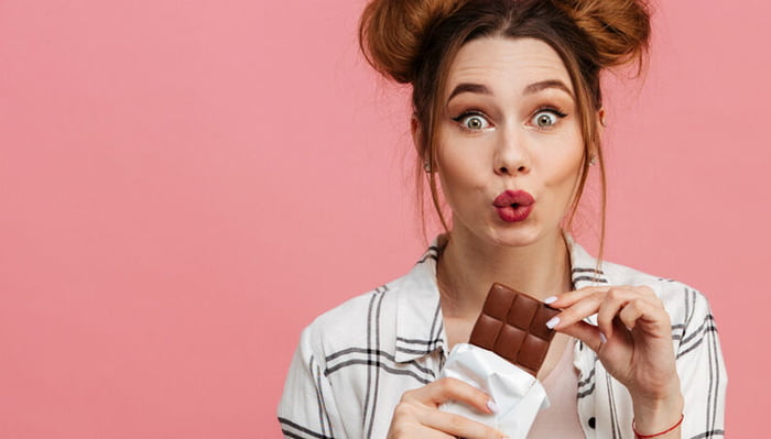 Imagem colorida de mulher comendo chocolate - Metrópoles