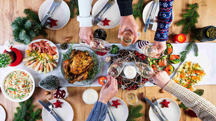 Imagem colorida em que aparece uma mesa e várias pessoas fazendo um brinde de Natal - Metrópoles