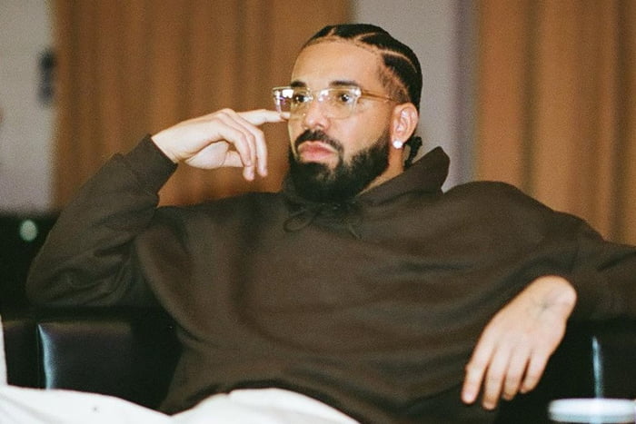 Foto colorida de Drake com a mão na cabeça e usando moletom e óculos - Metrópoles