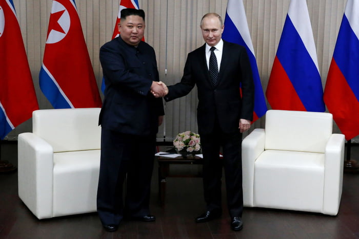 Imagem colorida mostra Kim Jong-un e Putin apertando as mãos em frente as bandeiras da Coreia do Norte e da Rússia - Metrópoles