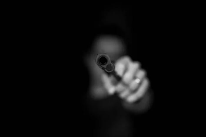 Imagem em preto e branco de homem apontando uma arma de fogo