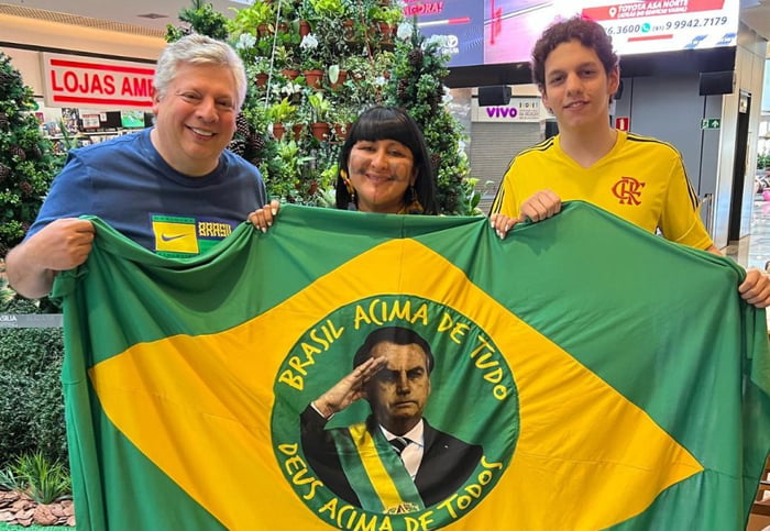 Imagem colorida mostra José Trabulo Junior, à esquerda de azul, segurando uma bandeira do Brasil com a foto de Jair Bolsonaro - Metrópoles