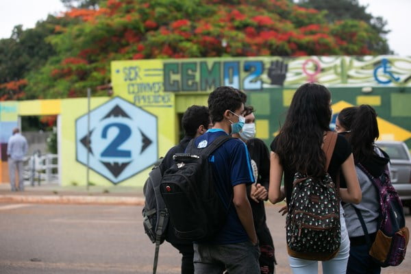 Fotografia colorida de adolescentes com mochila parados em frente a escola