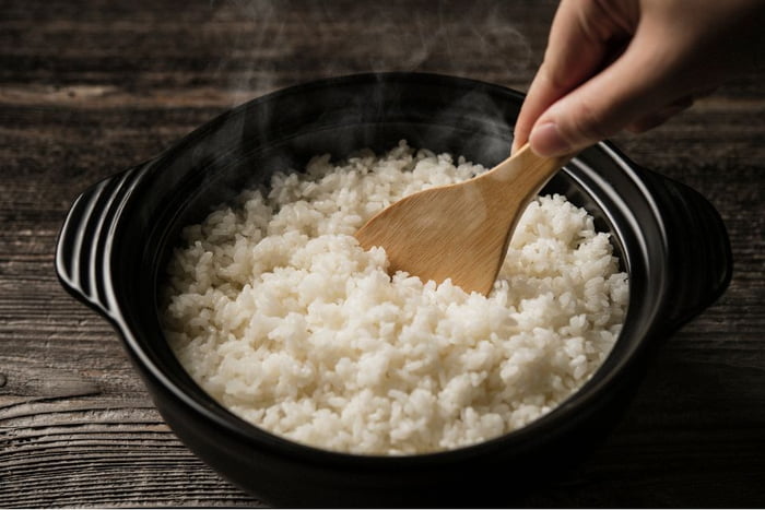 Foto de pessoa segurando colher de pau em prato de arroz