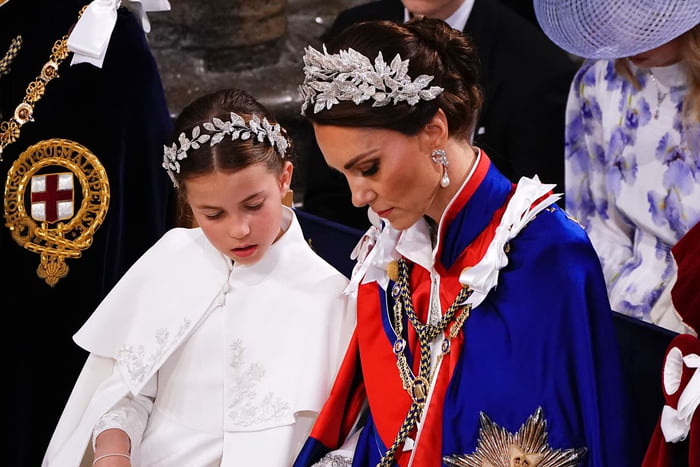 Foto colorida de menina e mulher, ambas brancas, com uma tiara na cabeça. A menina usa uma roupa branca, enquanto a mulher está com uma capa vermelha e azul, com medalhas - Metrópoles