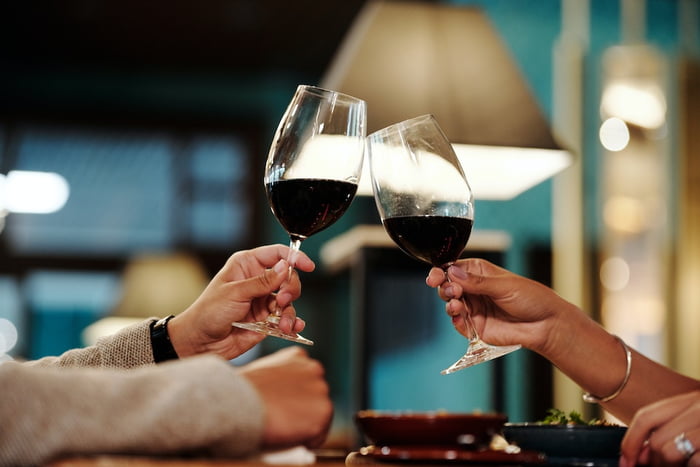 Na foto, duas pessoas brindam com uma taça de vinho