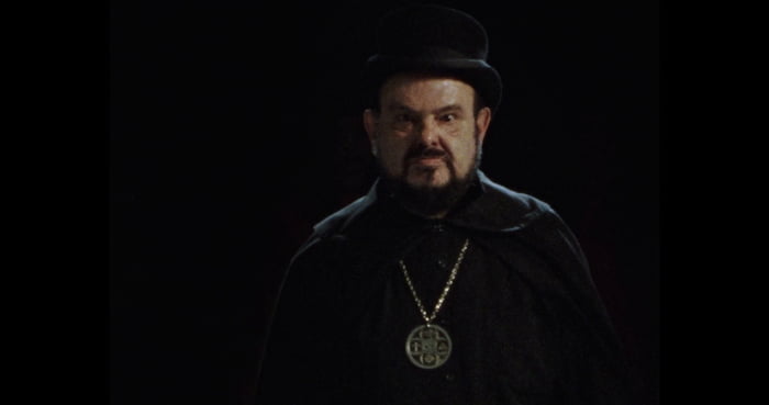 Foto colorida do filme A Praga, de Zé do Caixão. Na imagem, ele está com uma cartola, roupa toda preta e colar - Metrópoles