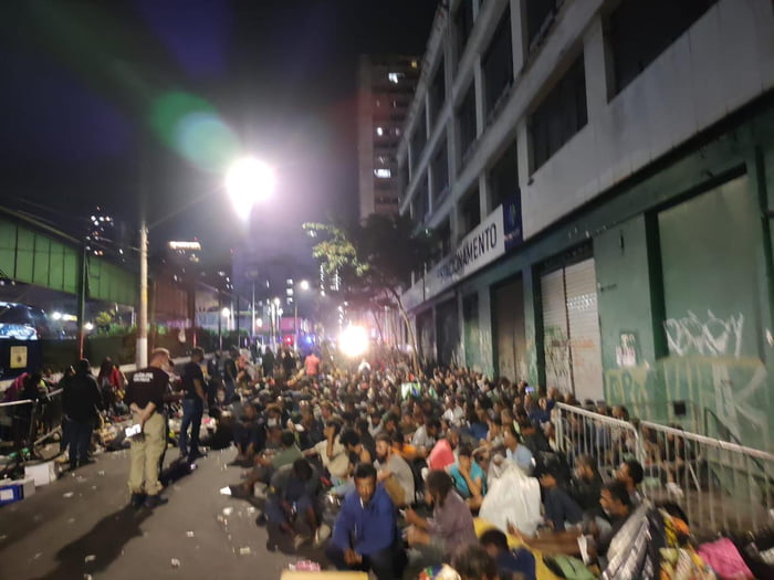 Fotografia à noite mostra grande número de pessoas sentadas na rua durante operação policial na cracolândia - metrópoles