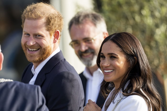 Foto colorida. Imagem mostra Harry, um homem branco, ruivo, e sua esposa, Meghan, uma mulher negra, cabelos pretos e lisos. Ambos estão sorrindo - Metrópoles