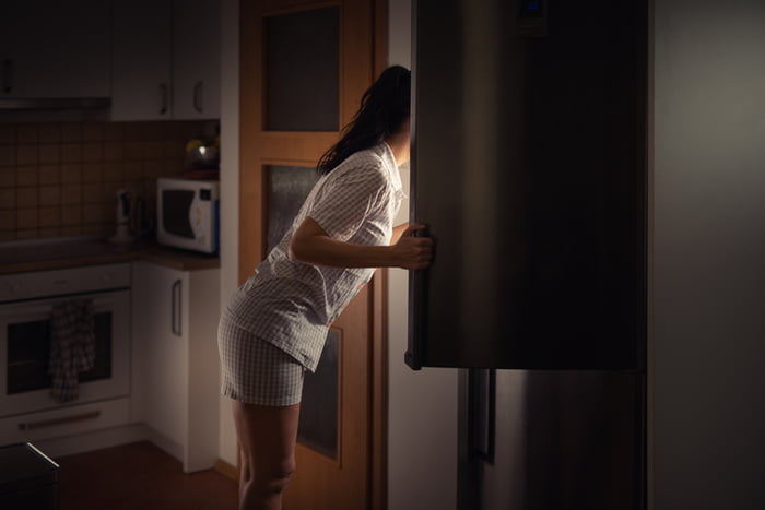 Foto mostra pessoa pegando lanches na geladeira com as luzes da casa desligadas