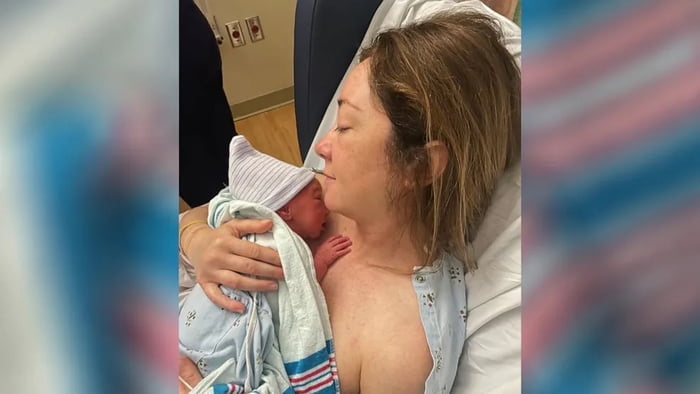 Foto mostra mulher em maca de hospital segurando em seus braços um bebê recém-nascido