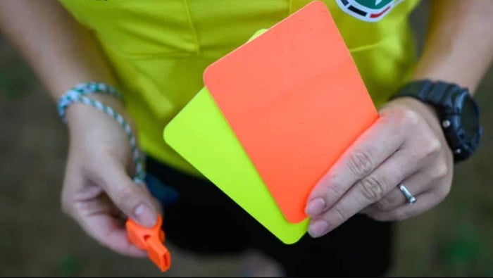 Imagem colorida de árbitro de futebol com cartões amarelos, vermelhos e apito na mão