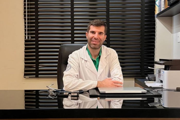 Foto mostra um médico sentado em um consultório usando jaleco e olhando a câmera - Metrópoles