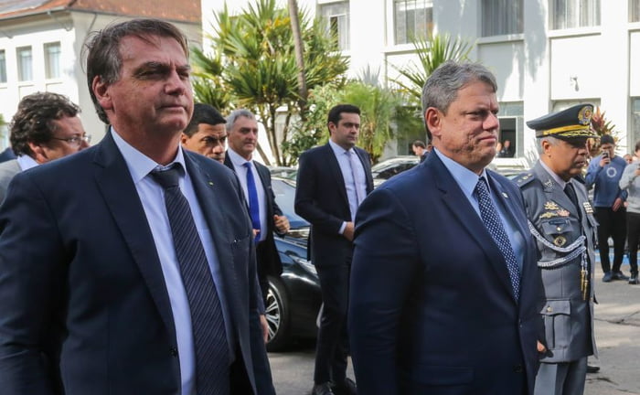 Imagem colorida do ex-presidente Jair Bolsonaro ao lado de governador Tarcísio de Freitas, ambos de terno de gravata em pé em evento de formatura da academia militar de são paulo - metrópoles