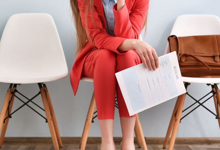 Mulher segurando curriculum na mão para vaga de emprego com terno vermelho sentada na cadeira - Metrópoles