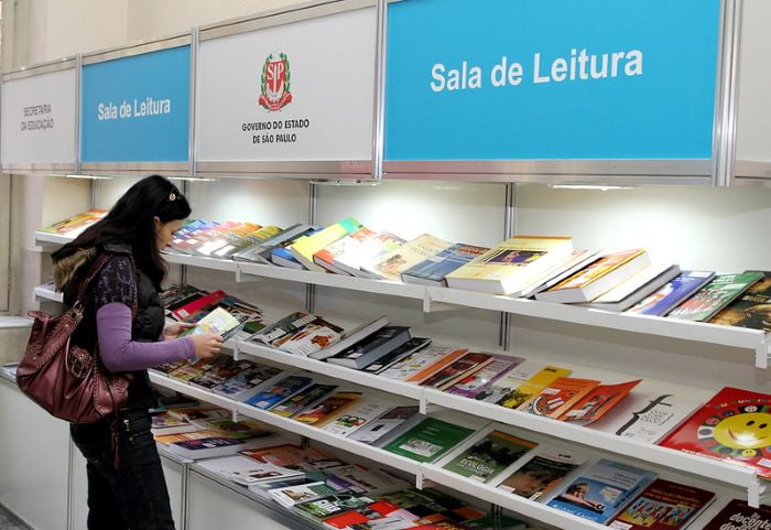 imagem colorida mostra mulher com livro na mão em frente à prateleira da sala de leitura do governo de são paulo - metrópoles