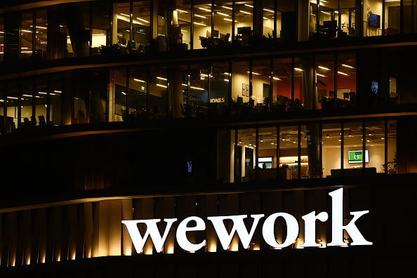 Imagem de escritório com o logotipo da WeWork em letras brancas e funcionários trabalhando com as luzes acesas em diversas salas - Metrópoles