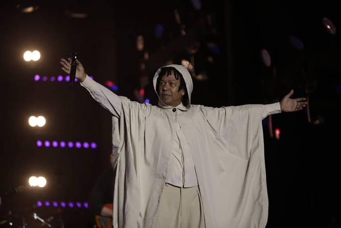 Foto colorida do cantor Djavan com roupa branca em um palco - Metrópoles