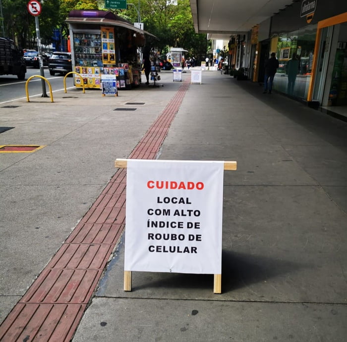 Foto colorida mostra placa posicionada em calçada com os dizeres: "Cuidado. Local com alto índice de roubo de celular" - Metrópoles