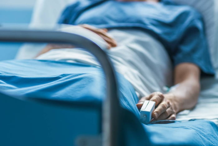 Imagem colorida de paciente deitado em maca de hospital com roupas azuis e medidor no dedo - Metrópoles
