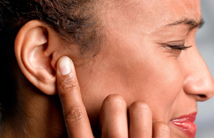 Mulher aperta o próprio ouvido com expressão de dor devido a um zumbido
