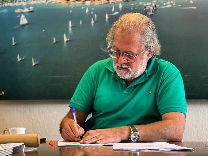 Fotografia colorida mostra prefeito de Ilhabela, Antonio Colucci, de camisa verde, e escrevendo sobre um papel - Metrópoles