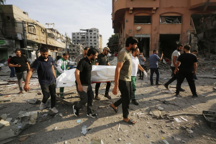Imagem colorida mostra Pessoas carregam um cadáver ao redor de edifícios destruídos e escombros no bairro de Al-Karama após um ataque aéreo de Israel que já dura cinco dias na Cidade de Gaza - Metrópoles