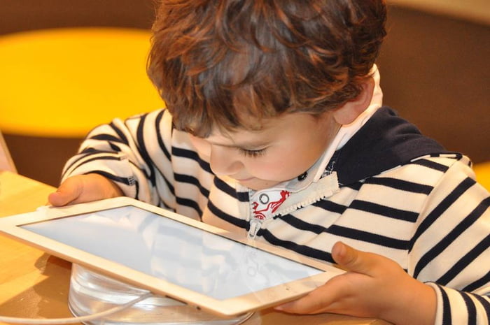Foto colorida de uma criança com blusa listrada segurando um tablet branco - Metrópoles