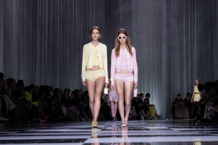 Na imagem com cor, duas modelos, com looks rosa e amarelo, desfilam para a Versace - Metrópoles