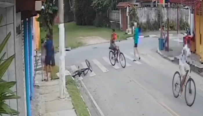 Imagem colorida mostra 3 bandidos de bicicleta abordando idosa no litoral de São Paulo. Um deles encosta a mulher em um muro de uma casa para roubar uma corrente - Metrópoles
