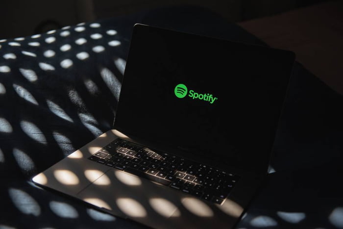 Foto colorida de um notebook no escuro com o símbolo do Spotify na tela - Metrópoles
