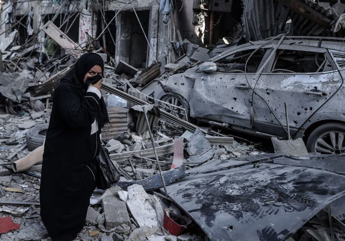 Imagem colorida de uma mulher ao redor de escombros de prédios em Gaza após ataques de Israel - Metrópoles