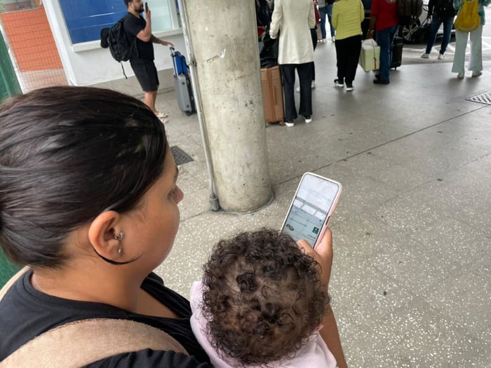 foto colorida de mulher com criança no colo tentando pegar carro de aplicativo em saguão da Estação Barra Funda em dia de greve - Metrópoles