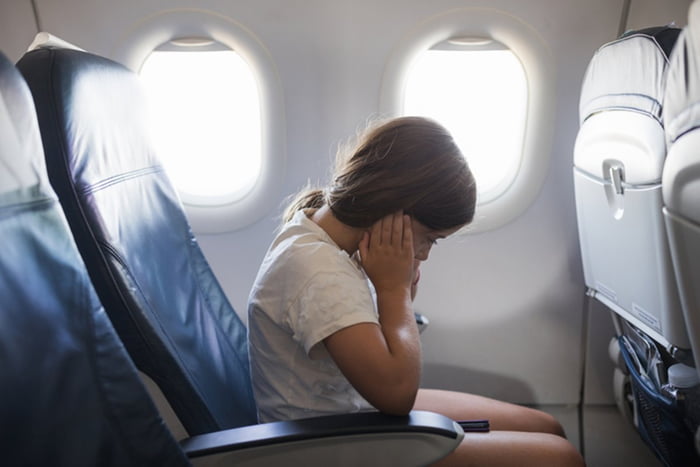 Menina com dor de ouvido no avião coloca mãos nas orelhas - Metrópoles