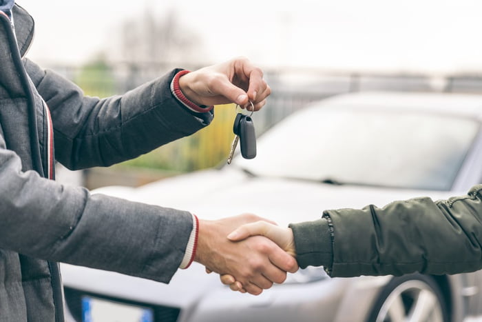 Imagem de dois homens se cumprimentando com as mãos, diante de um carro. Um deles entrega a chave do veículo para o outro - Metrópoles