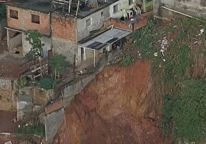 Imagem colorida mostra barranco em que houve deslizamento e casas ao lado