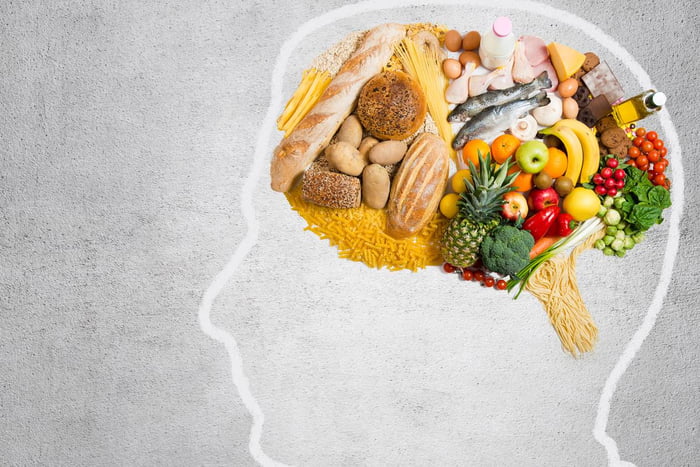 Foto do rosto de um homem desenhado em um quadro cinza. Vários alimentos fazem o formato do cérebro dentro da cabeça desenhada - Metrópoles