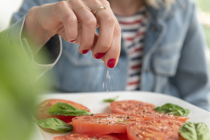 Fotografia mostra mulher de unhas vermelhas colocando sal em um prato de tomates - Metrópoles