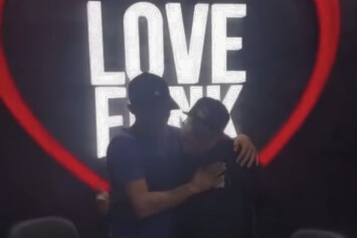 Imagem colorida de homens se abraçando em frente a luminoso no qual está escrito love funk - Metrópoles