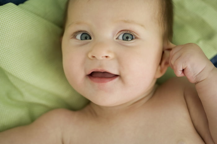 Imagem mostra bebê de pele e olhos claros sorrindo e puxando uma das orelhas - Metrópoles