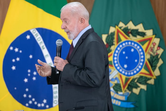 Imagem colorida de presidente Lula em pé segurando microfone em frente à bandeira do Brasil - Metrópoles